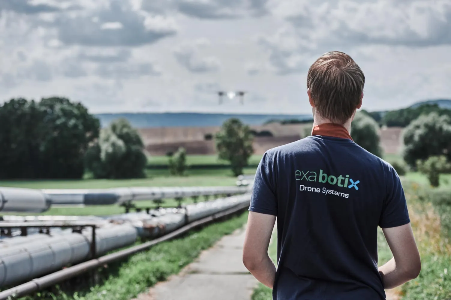 Exabotix employee controls drone in the distance over a pipeline running through an uninhabited landscape.